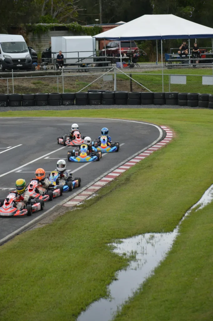 Six young drivers in helmets racing go-karts through a track corner