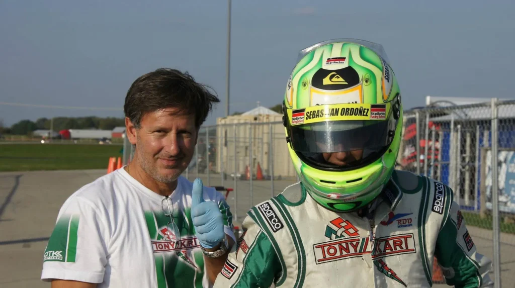 VMotorsport coach standing trackside with a driver in helmet and race suit
