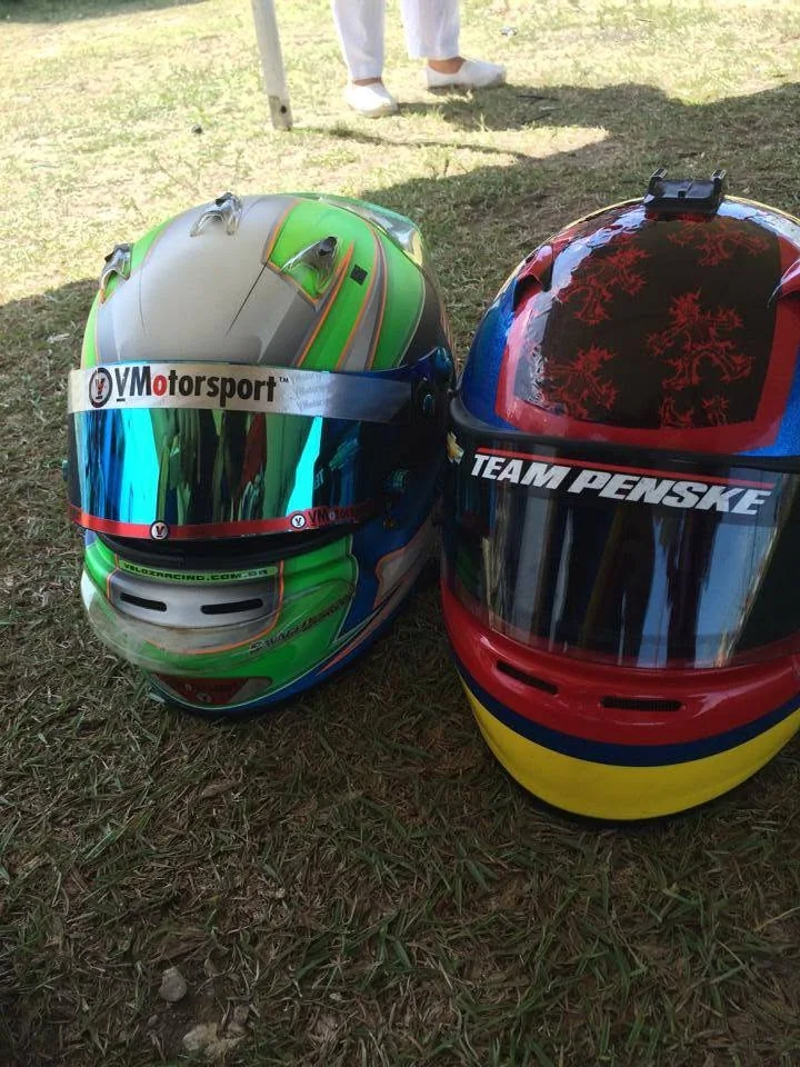 Two racing helmets on the grass, one carrying VMotorsport graphics