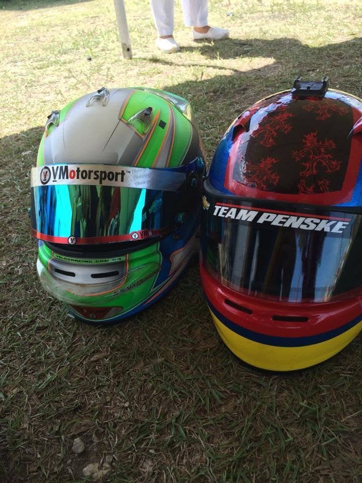 Two racing helmets resting on the grass, one with a VMotorsport visor graphic