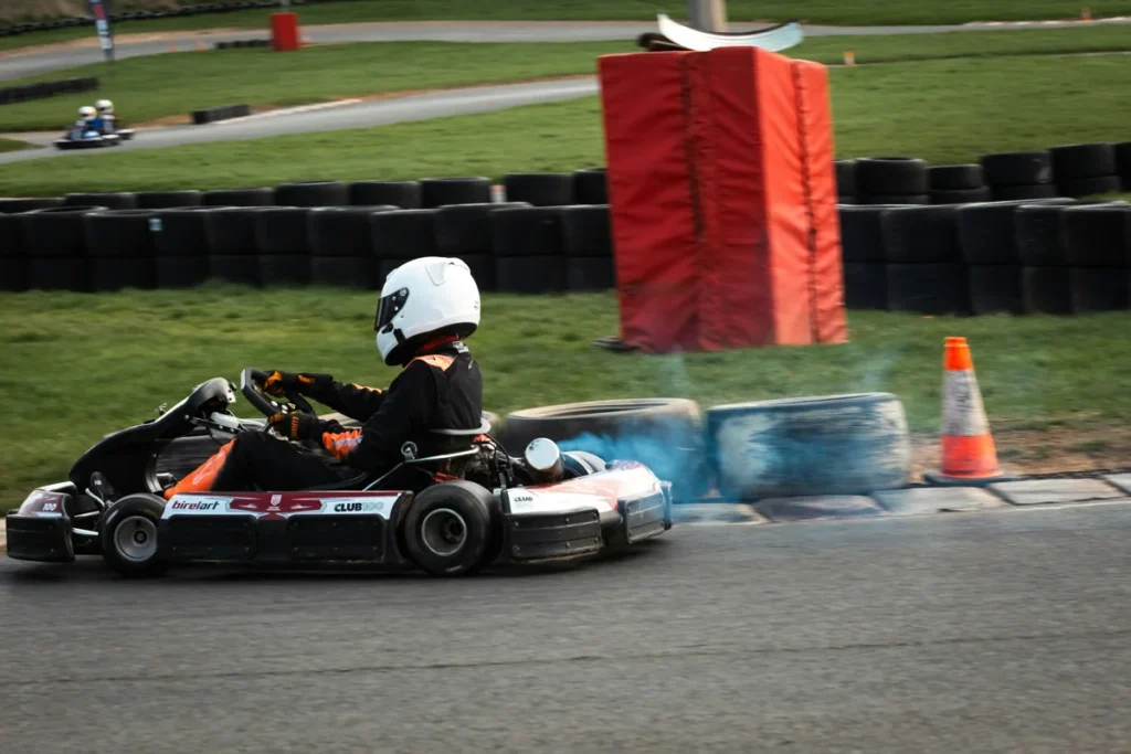 Driver in a white helmet and black race suit taking a corner in a go-kart
